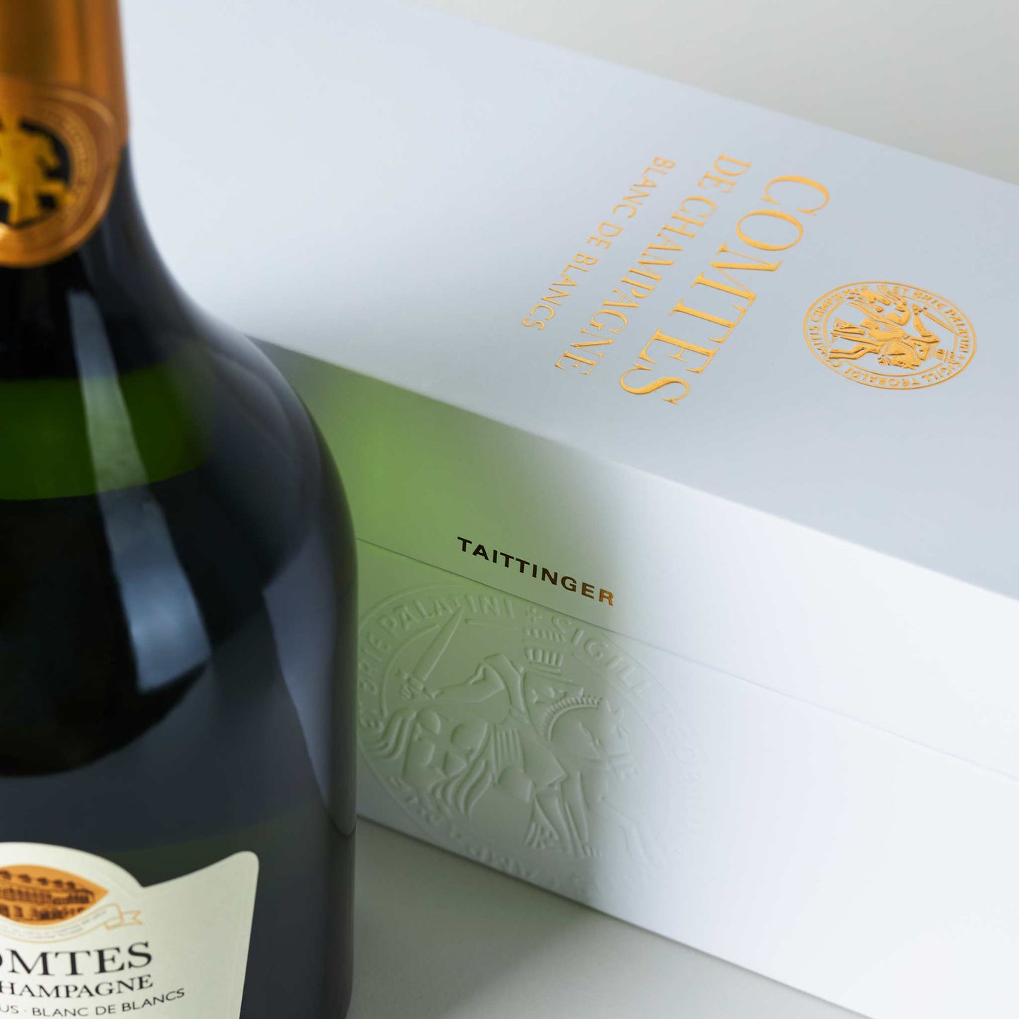 Champagnerflasche stehend vor weißem Tattinger Transportkarton mit goldener Aufschrift