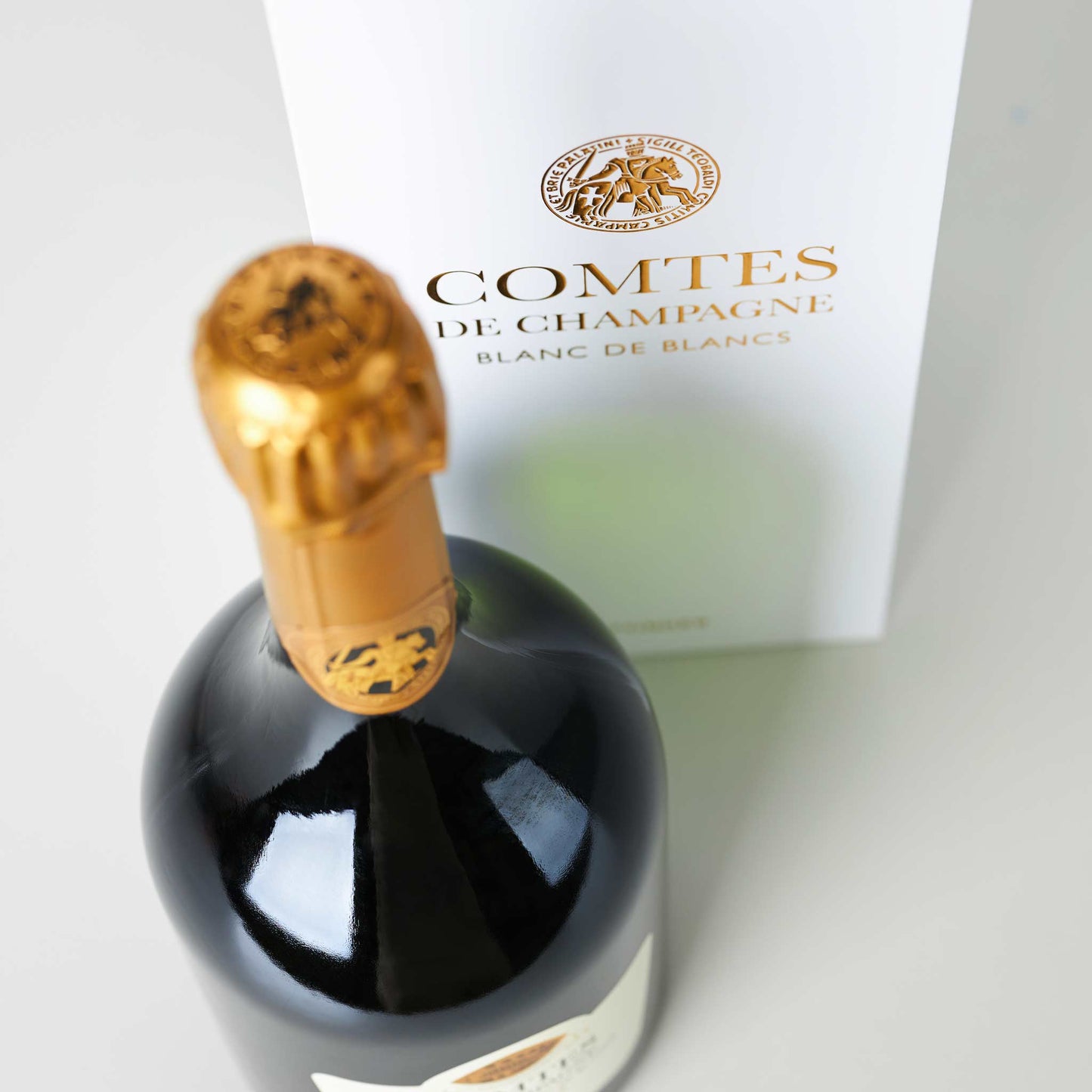 Champagnerflasche stehend vor weißem Tattinger Transportkarton mit goldener Aufschrift
